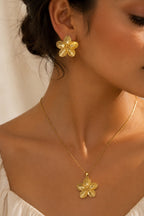 A close-up lifestyle shot of a model wearing a matching gold flower-shaped stud earring and necklace with a textured gold flower pendant.